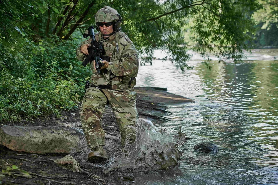 Soldier in full uniform running through river with gun in hand