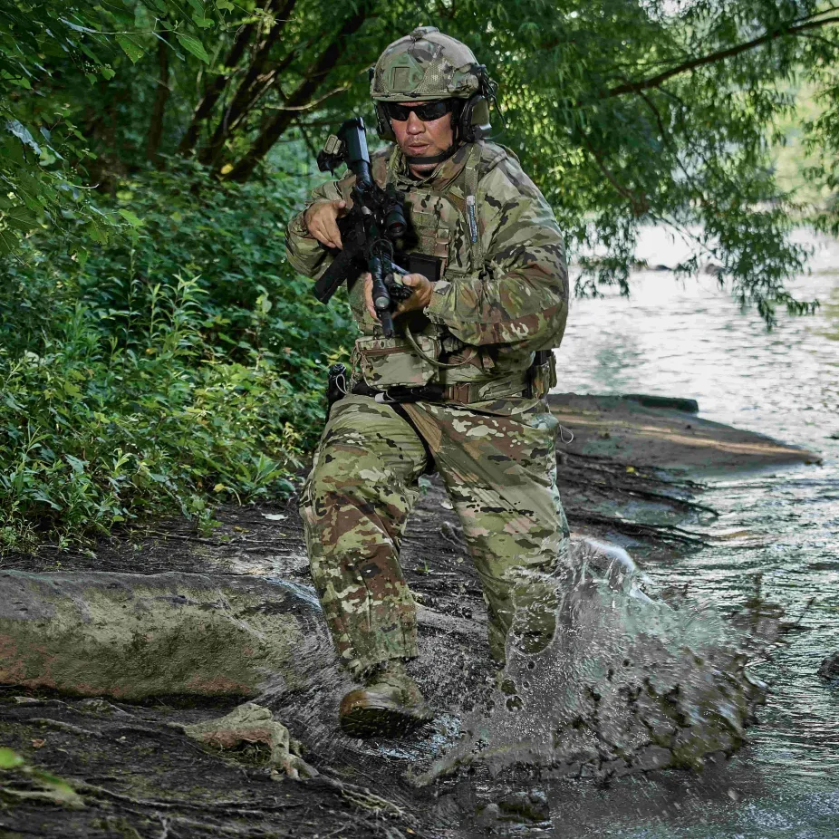 Soldier in full uniform running through river with gun in hand